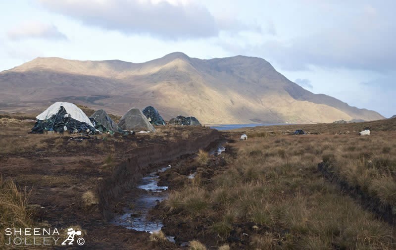 This shot was taken in Galway in Ireland. These are piles of freshly cut turf. The water is Lough Inagh and beyond are the Maumturk Mountains.
