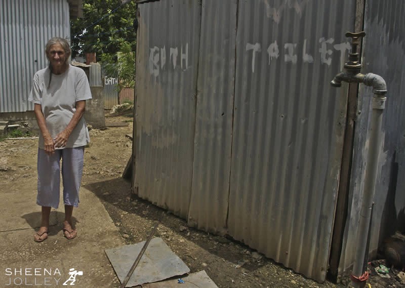 Louise in back yard. The shower and toilet are enclosed by a corrugated iron structure. The outside tap is also used for washing.