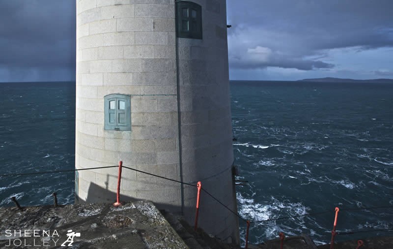 A close up of the structure of the fastnet lighthouse showing the blockwork. A tense moment as an approaching storm is looming turning the clouds an inky blue and whipping up the ocean waves.